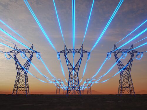 Steel transmission towers stretch across a desert plain at sunset while glowing blue strands symbolize data-intensive artificial intelligence increasing power consumption.