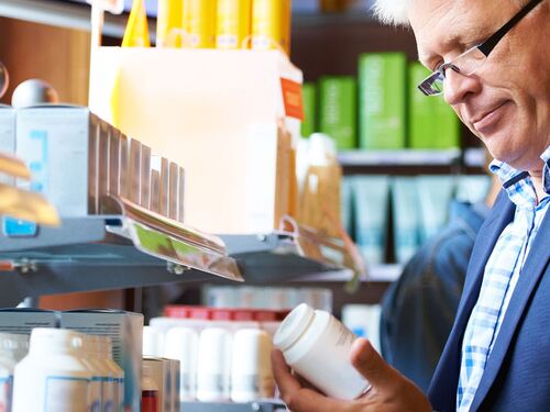 A man reading the information on a bottle of supplements in a store