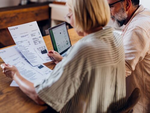 Senior couple carefully reviewing their household energy bill together on a laptop at home. They seem focused and concerned.
