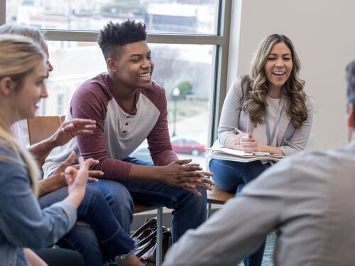 A group of young adults sitting in a circle smiling and talking to each other.