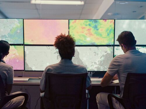 Weather, screen and meteorology with people for forecast, satellite maps or teamwork to track storm. Control room, back or scientists with monitor for broadcast news, pattern review or climate change.
