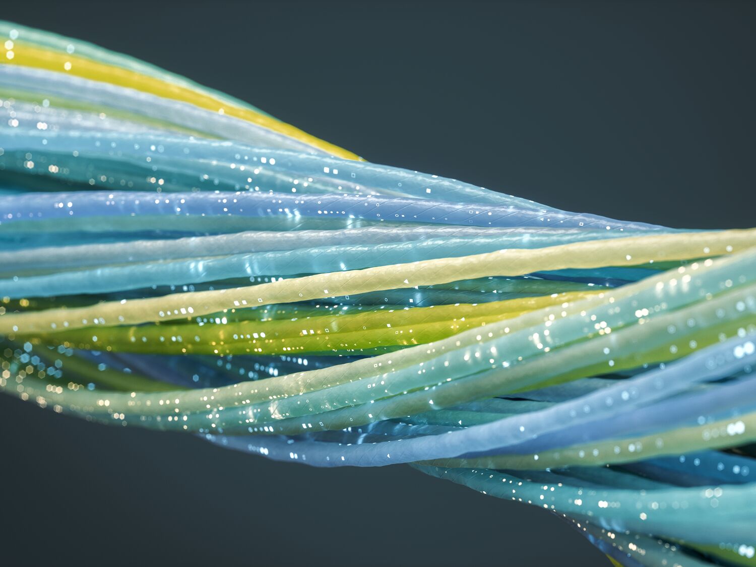 Twisted strands of light blue, green, and yellow cables against a dark background. Glowing white specks run along the length of the strands, representing data transfer or network connectivity. photo by imaginima for iStock