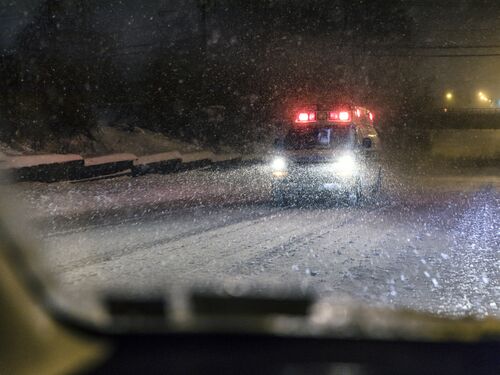 A medical emergency services vehicle ambulance is speeding - responding to an urgent call with blinding headlights, flashing emergency lights and shrieking siren - as it approaches on an urban street during a night time raging blizzard snow storm near Rochester, New York State, USA.