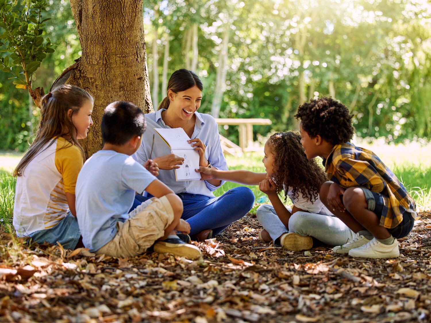 Shot of a teacher reading a book to her class in a park