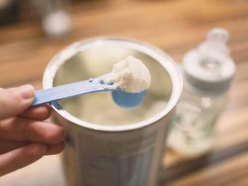 Powder milk for baby and blue spoon on light background close-up. Milk powder for baby in measuring spoon on can. Powdered milk with spoon for baby. Baby Milk Formula and Baby Bottles. Baby milk formula on kitchen background