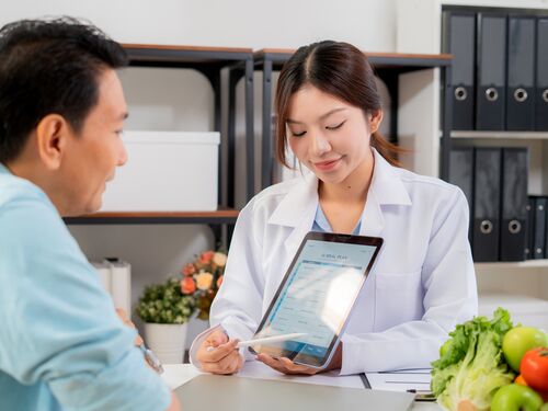 Asian nutritionist using tablet to explaining personalized meal plan with AI to patient during healthcare consultation, healthy lifestyle, woman dietitian showing nutrition plan with AI on tablet.