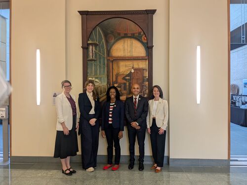 Five New Voices members standing in front of a mounted artifact.