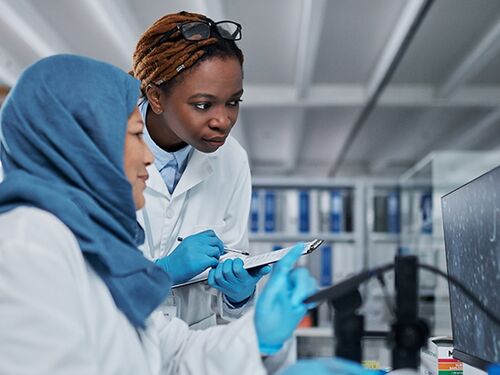 Two researchers in lab coats review data on a computer screen in a laboratory.