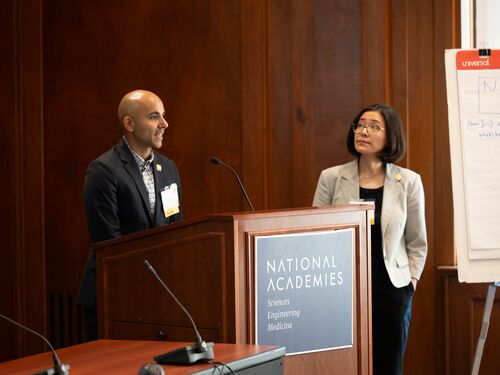 Two people standing at a podium, speaking and presenting to an audience.