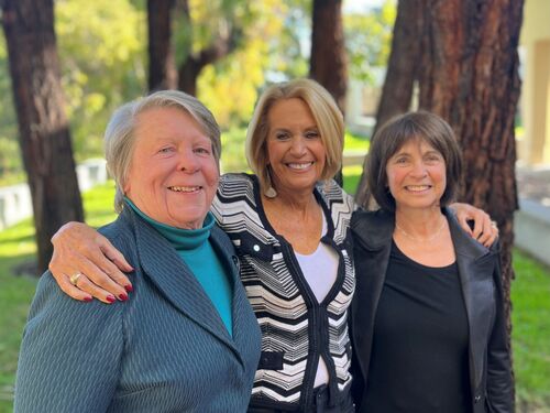 Diane Griffin, Marcia McNutt, and Susan Wessler stand together in front of five trees. Marcia has her arms around the shoulders of Diane and Susan.