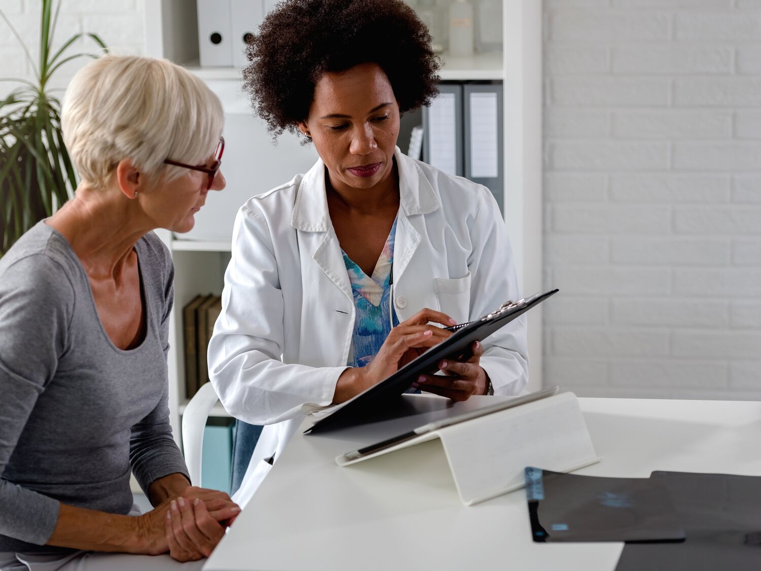 A female doctor sits at her desk and chats to an elderly female patient while looking at her test results.