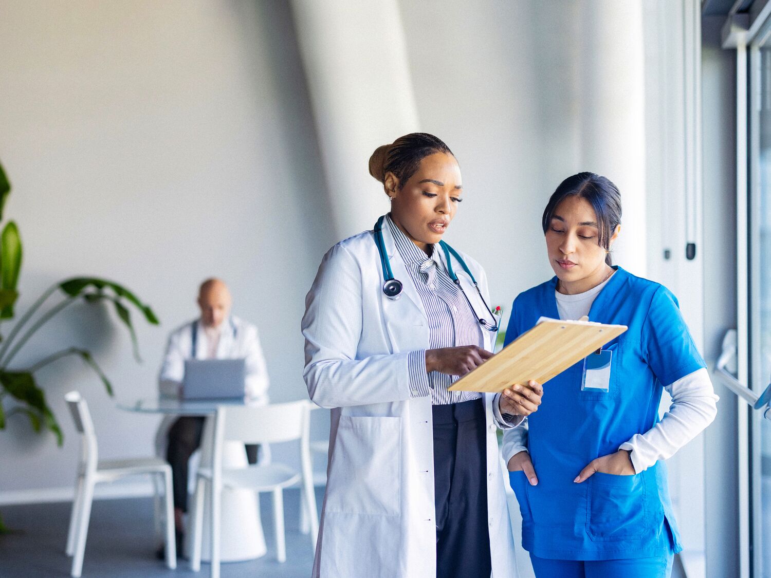 Doctor and nurse review a patient chart together in a bright hospital corridor, collaborating on care.