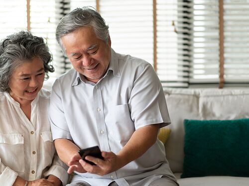 Elderly couple smiling looking at smart phone.