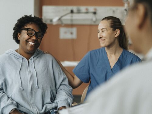 Smiling female nurse consoling happy patient sitting with doctor during consultation at hospital