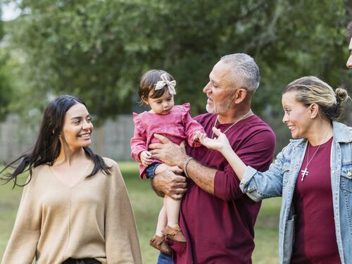 A multi-generation Hispanic family standing in the park together.