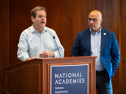 Two New Voice members standing at a podium speaking to a room of individuals.