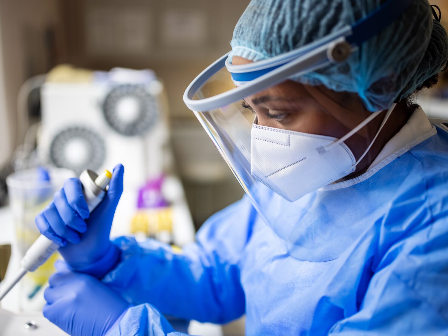 A person wearing a full PPE suit, face mask, and face shield working with pathogen samples in lab.