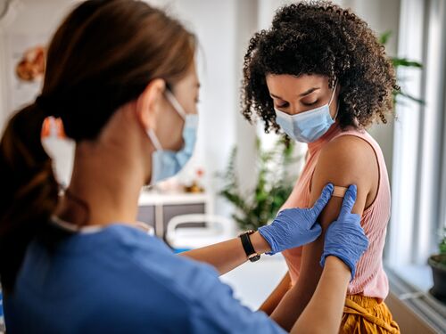 Photo of nurse putting adhesive bandage on young woman patient’s arm after vaccination at a clinic. Vaccination for covid-19.