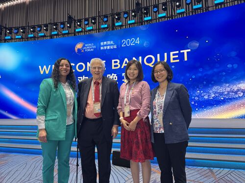Three New Voices members standing next to Dr. Bruce Alberts at the World Laureates Forum.