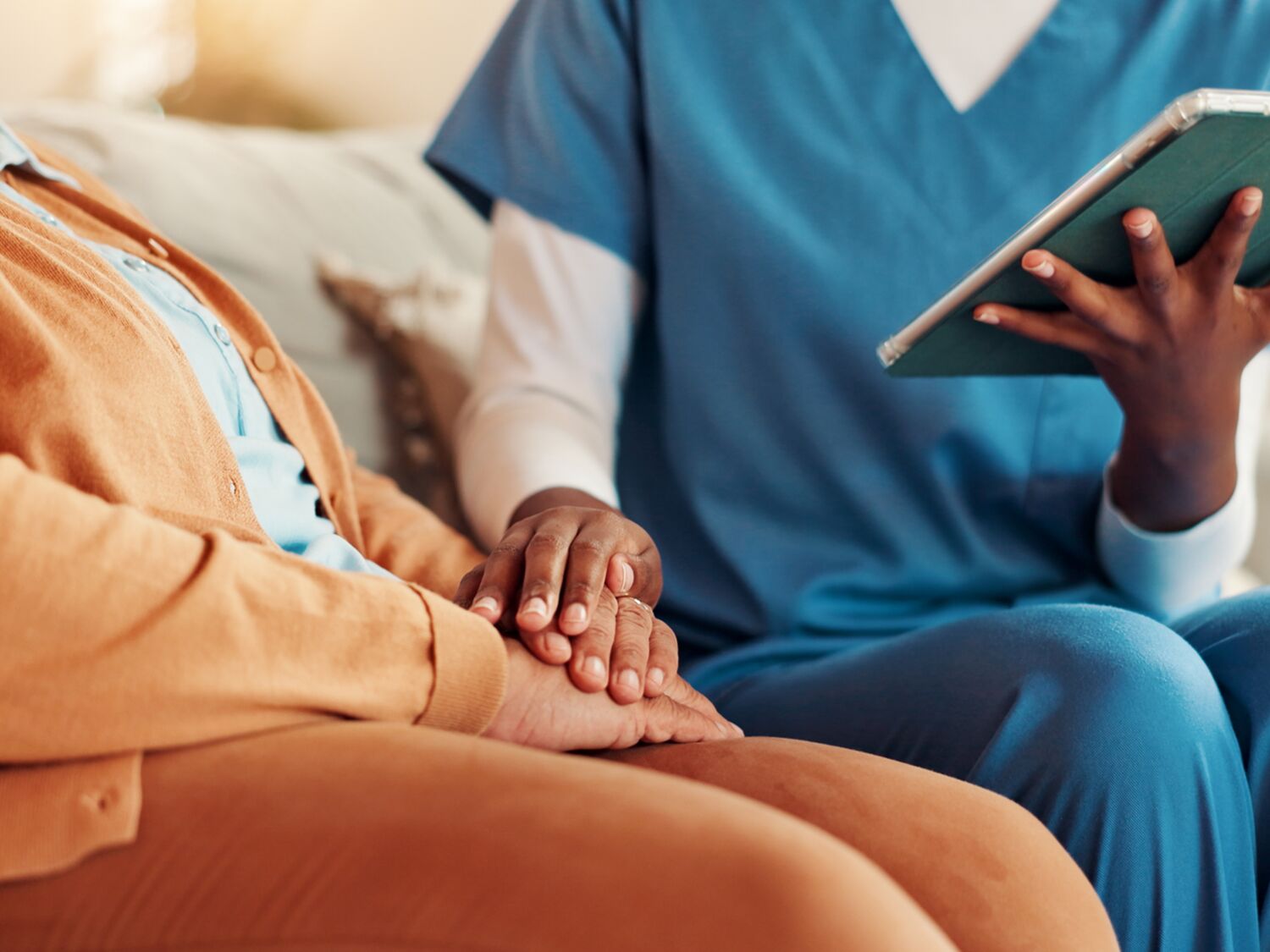 A nurse holding a tablet and placing her hand on a patient’s hands.