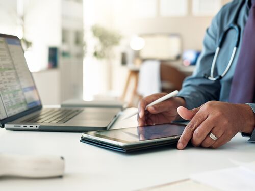 A doctor using a tablet and laptop.
