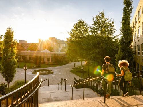 Rear view of two university students walk down campus stairs at sunset.