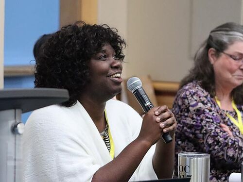2 women panelists speaking at a meeting, one holding a microphone