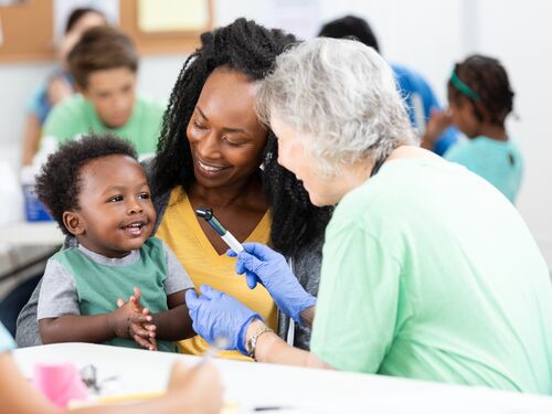 A healthcare worker in gloves interacts with a young child and their mother.