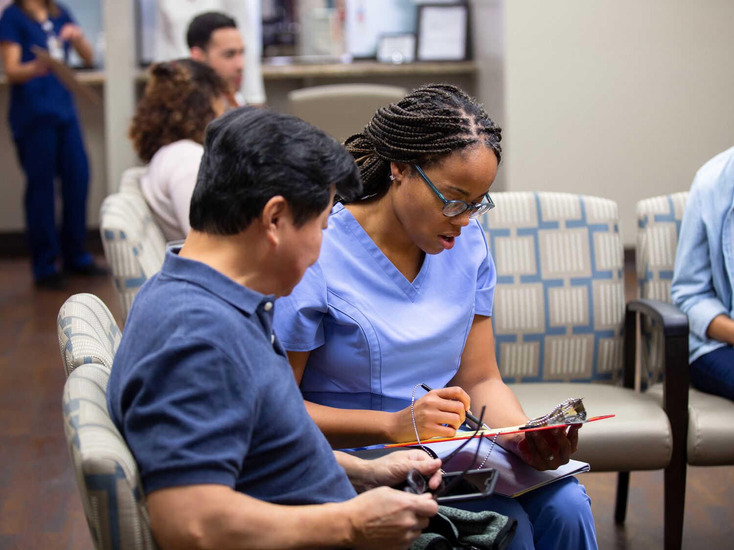 Healthcare worker assists patient, reviewing documents.  Medical clinic waiting room setting.