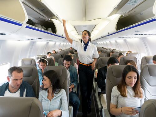 Happy flight attendant walking the aisle in an airplane closing overhead compartments