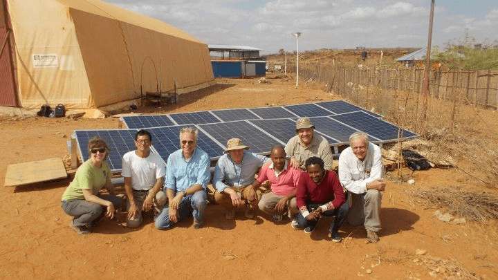 Group of people standing in front of solar panels in desert terrain.