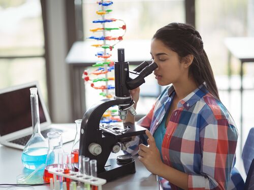 Attentive schoolgirl looking through microscope in laboratory