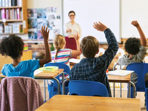 Shot of an unrecognizable group of children sitting in their school classroom and raising their hands to answer a question