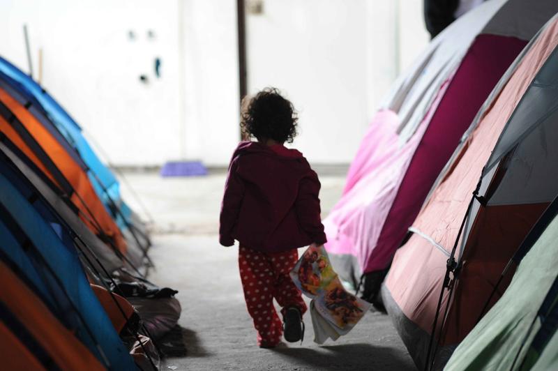 A child carrying a book walking between tents in an immigration detention center