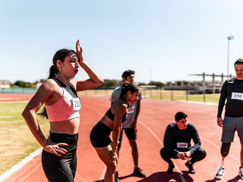 Tired young athlete woman taking a break after running on the sports track