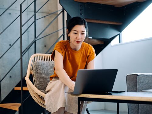 Young Asian woman using laptop and surfing the net in the living room at home. Freelancer, self-employment. Working from home. Relaxation. Lifestyle and technology